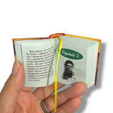 Miniature book held open by a hand with 'Capítulo 2' page displayed. La Metamorfosis