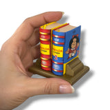 Hand holding a miniature book set with colorful spines on a white background. Mafalda