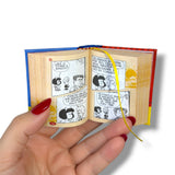 Miniature open book with comic pages held by a hand against a white background Mafalda
