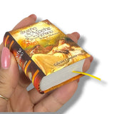 Hand holding a miniature book titled 'Sueño de Noche de Verano' with a romantic illustration on the cover.
