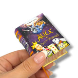 Hand holding a miniature book titled 'Alice nel Paese delle Meraviglie' with colorful illustrations on a white background.
