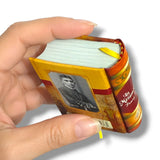 Hand holding a miniature book with a portrait on the cover against a white background  La Metamorfosis