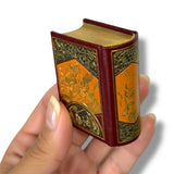 Hand holding a miniature ornate book with intricate designs on a white background