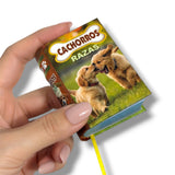Hand holding a small book with dog illustrations and text on a white background. Cachorros Razas