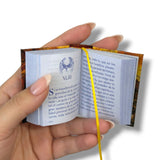 Hand holding a small open book with text and a logo on a white background. El Anticristo