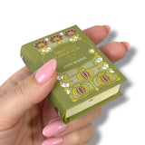 Hand holding a miniature book with decorative cover against a white background Orgullo y Prejuicio