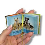 Hand holding a small open book with images of dogs on each page.Cachorros Razas