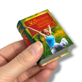 A hand holding a miniature book titled '365 Messaggi per l'Armonia e la Prosperità' against a plain white background.