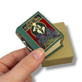 Hand holding a miniature book titled 'Peter Pan' with a colorful cover design.