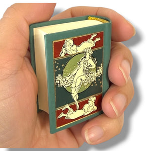 Hand holding a small book with decorative cover featuring women in classical poses. Peter Pan
