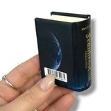Miniature book with 'Frankenstein' cover held by a hand on a white background