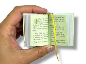 Hand holding a small open book with text and illustrations on a white background