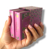 Hand holding a set of pink books with decorative covers on a white background. Sentido y Sensibilidad
