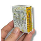A hand holding a miniature matchbox-style box with a white and yellow illustrated cover and a yellow spine labeled 'HUFFLEHUFF'.