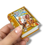 Miniature book held by a hand with colorful illustrations on the cover