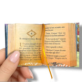 Miniature book held open by a hand with a decorative ribbon.