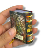 Hand holding a small decorative book with intricate designs and text.