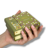Hand holding a stack of green books with floral patterns on a white Orgullo y Prejuicio background