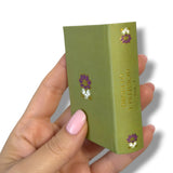 Hand holding a green book with floral design on a white background Orgullo y Prejuicio