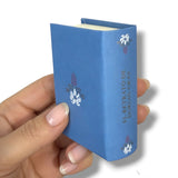 Hand holding a blue book with decorative cover against a white El Retrato de Dorian Graybackground
