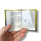 Hand holding a small open book with text and a drawing on a white background