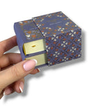 Hand holding a small, patterned box with a candle inside on a white background
