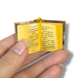 Miniature open book of Salmos held between fingers with visible text on a white background