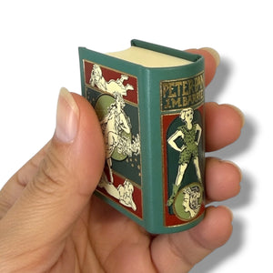 Hand holding a small book with vintage-style illustrations on a white background. Peter Pan
