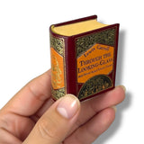 Miniature book titled 'Through the Looking-Glass' held in a hand against a white background