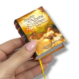 Miniature book held by a hand with a colorful cover featuring artwork and text. Sueño de una noche de Verano William Shakespeare