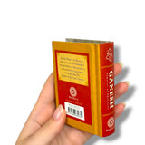 Hand holding a miniature book titled 'Ganesh' with a red and gold cover.