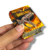 A hand holding a miniature hardcover book titled 'DINOSAURI' with a detailed illustration of a T-rex on the cover, set against a plain white background.
