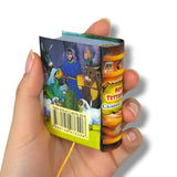 Hand holding a small book with colorful illustrations on a white background