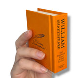 Hand holding an orange book titled 'William Shakespeare' on a white background