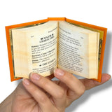 Miniature book held open by a hand with visible text on a white background