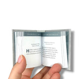 Hand holding a small open book with text on a white background