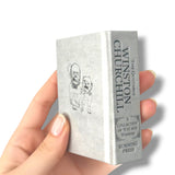 Hand holding a miniature book titled 'The Quotable Winston Churchill' on a white background