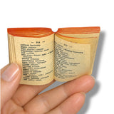 Small book-shaped package with text held by a hand against a white background