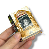 Miniature book titled 'Sacre Bible Illustree' held by a hand on a white background