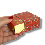 Hand holding a red patterned chocolate box with a white background. La Edad de la Inocencia