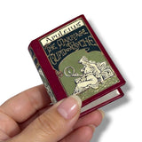 Miniature book titled 'The Marriage of Cupid and Psyche' by Apuleius held in a hand against a white background