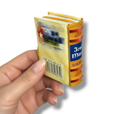 Hand holding a small book-shaped container with colorful design and 'Joss & Main' branding.Jose Marti