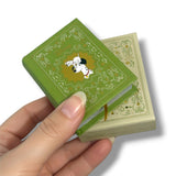 Hand holding a small green book with a dog illustration on a white background 102 Dalmatas