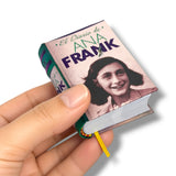 A hand holding a miniature book replica of 'El Diario de Ana Frank' against a clean white background.