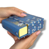 Hand holding a blue floral-patterned book-shaped container with a yellow El Retrato de Dorian Grayinterior.