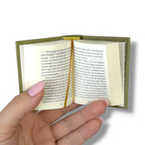 Hand holding a small open book with text on a white background Orgullo y Prejuicio