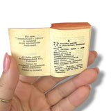 Miniature book held open by a hand with pink nail polish on a white background Lilliput Dictionary