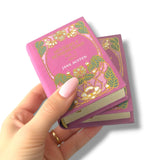 Hand holding a miniature book with decorative cover on a white background. Sentido y Sensibilidad