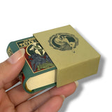 Hand holding a small book with a green cover and gold decorative elements, open to reveal another book inside. Peter Pan