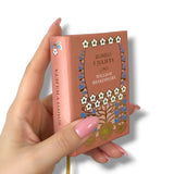 Hand holding a miniature book titled 'Romeo y Julieta' by William Shakespeare with decorative cover.